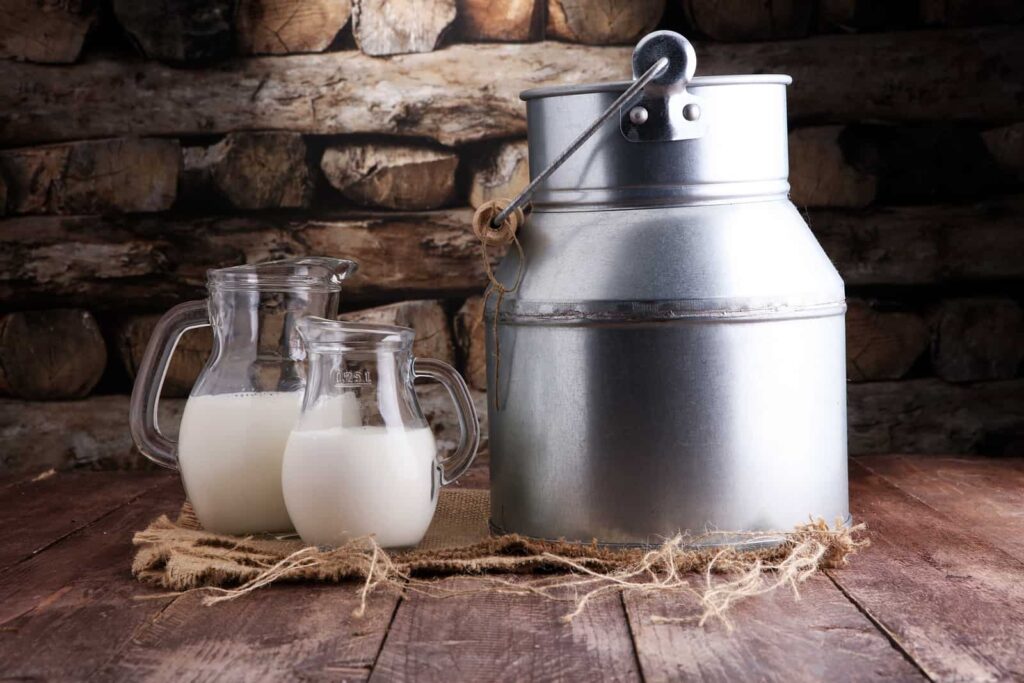 A jug and glasses of pasteurized milk sitting on a wooden table