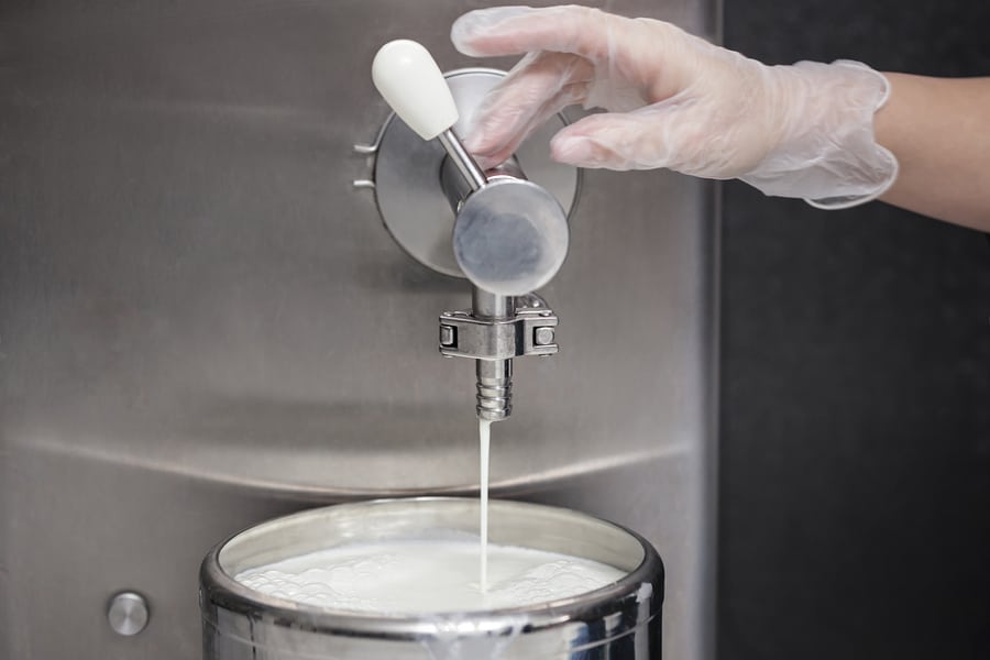 A worker filling a container up with milk from a tank at a factory.