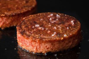 A plant-based burger patty seasoned with salt being cooked on a grill. 