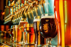 A line of different draft beers being filled from the tap on a bar. 