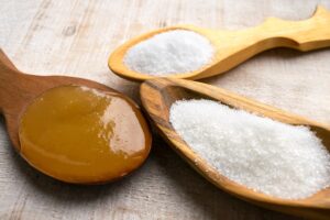 Three wooden spoons on a table each holding a different artificial sweetener. 